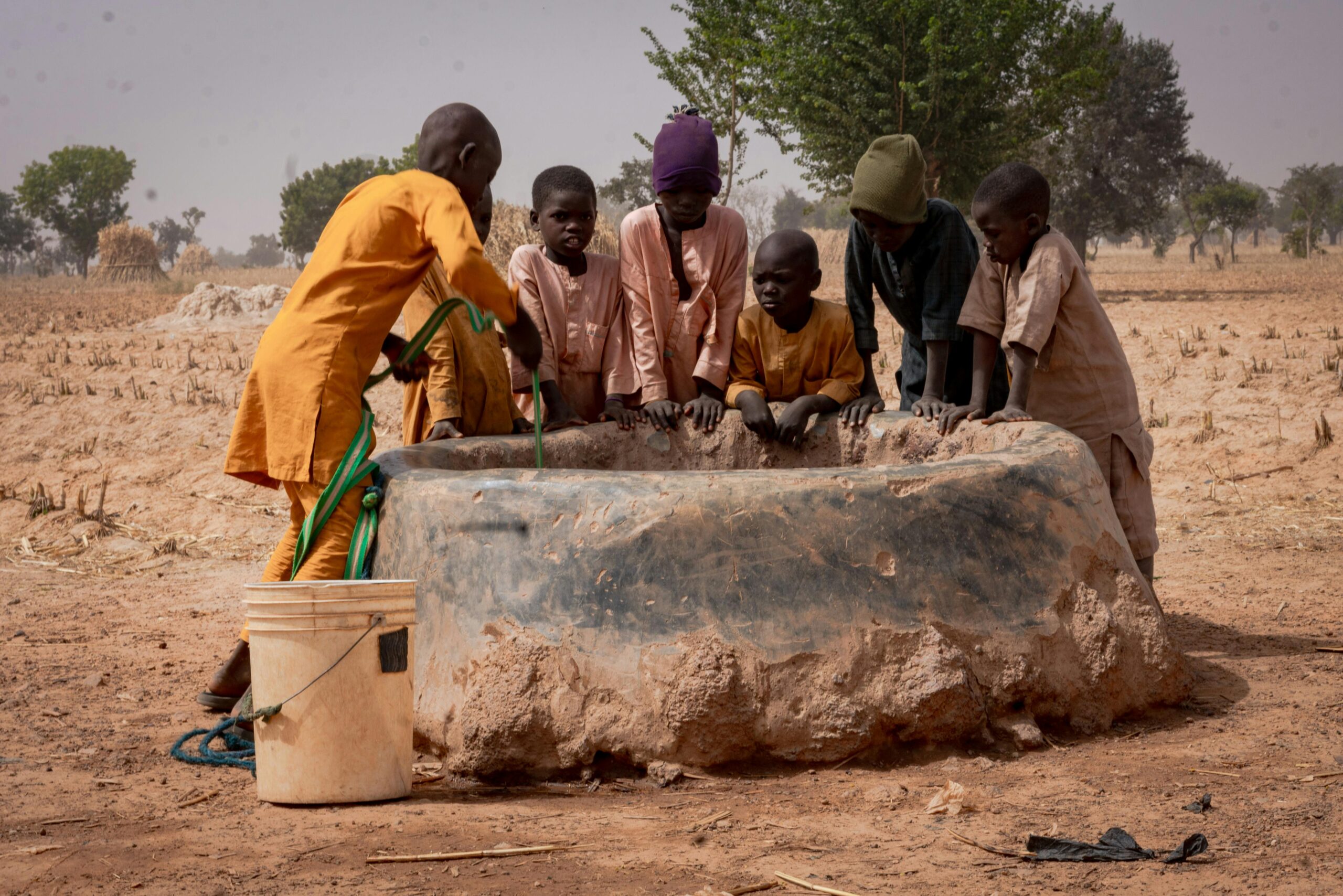 Offerings Group of children fetching water from a well in a rural landscape.